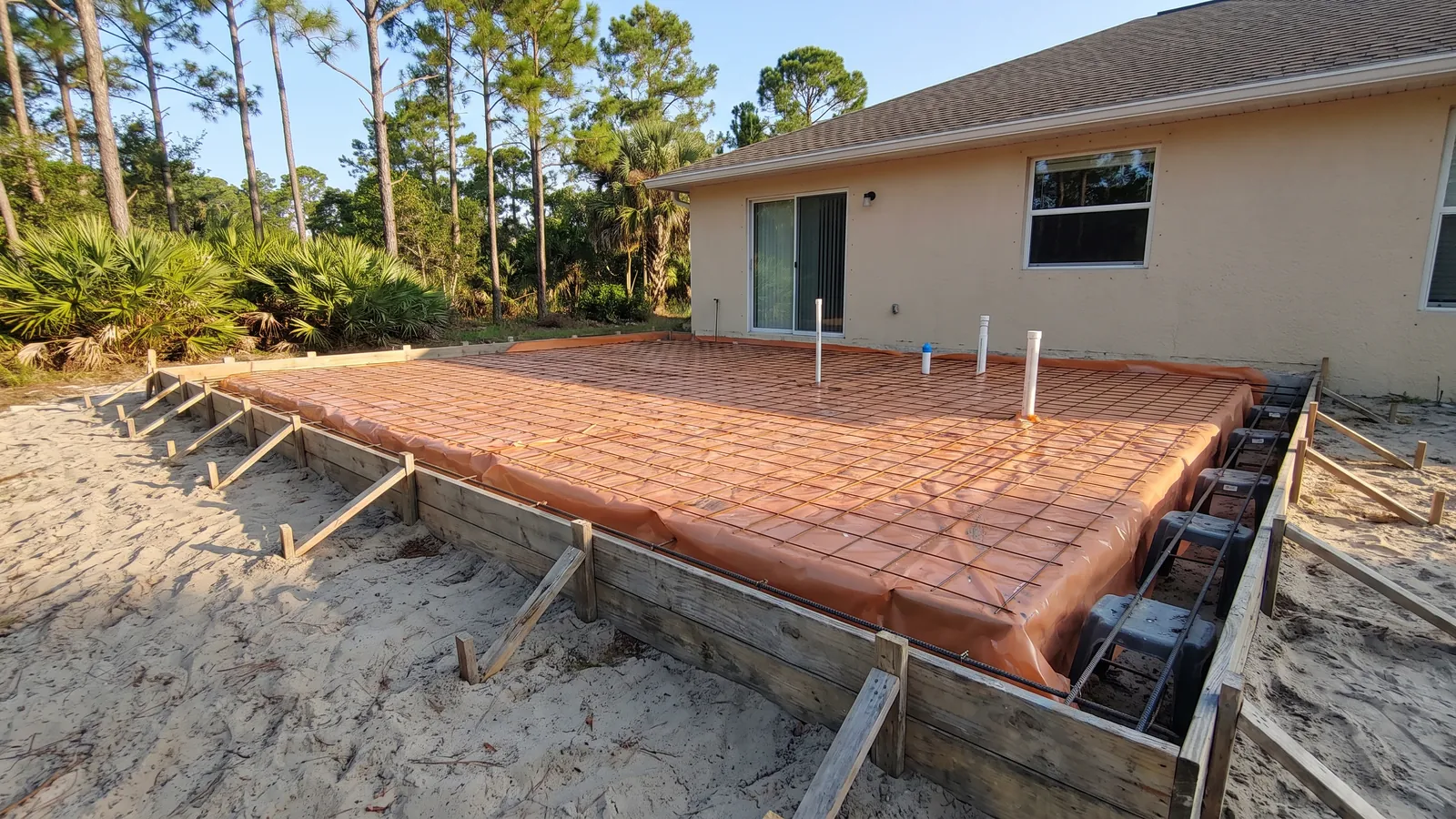 Monolithic slab foundation with thickened-edge footing forms, rebar chairs and vapor barrier ready for a pour in Florida sand